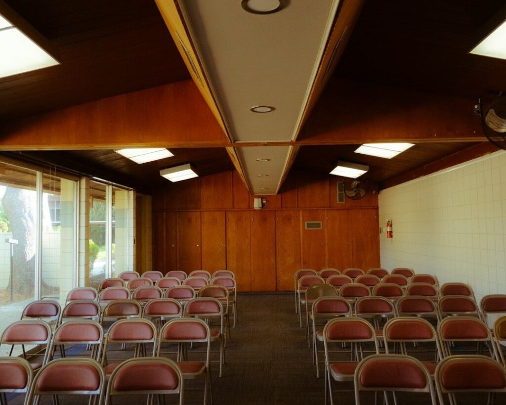Lege zaal met rijen stoelen, brede doorgang en nooduitgangdeur